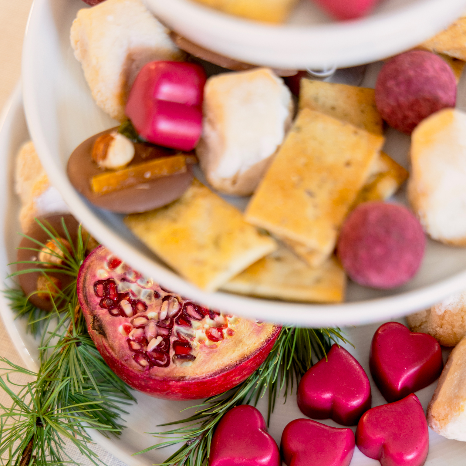 Close-up of Thomas White's cake stand, filled with various cookies, red chocolates, half a pomegranate, and pine branches